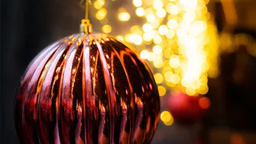 Eine glänzende Weihnachtskugel schwingt vor leuchtendem Hintergrund.