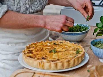 A quiche is decorated with fresh herbs in a kitchen.