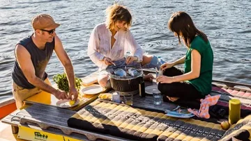 Three people cook relaxing on a boat on the water.