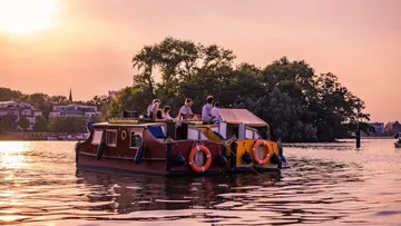 A houseboat sails quietly on a body of water at sunset.