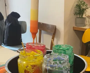 Bunte Kerze tropft Farbe in Glasbehälter auf Tisch.