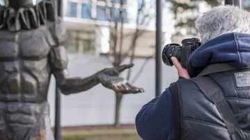 Photographer holds camera while taking pictures of a statue.