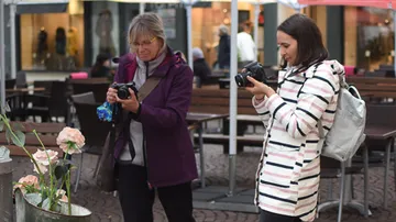Two women take pictures of flowers in a café.