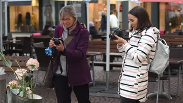 Two women take pictures of flowers in a lively café.
