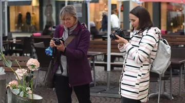 Two women take pictures of flowers in a café.