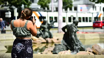 Frau fotografiert mit Kamera Skulpturen neben einem Brunnen.