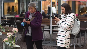 Zwei Frauen fotografieren Blumen in einer belebten Umgebung.