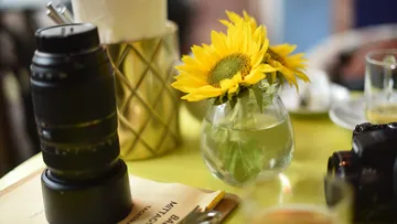 Kameraobjektiv nebeneinander mit Sonnenblume in einer Vase.
