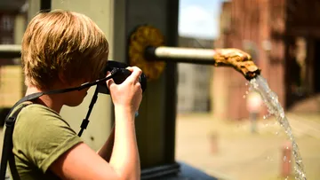 Ein Junge fotografiert sprudelndes Wasser aus einem Brunnen.