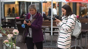 Two women take pictures of blooming plants outdoors.