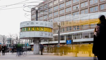 Clock shows departure times, people move around them.