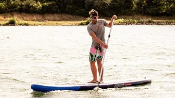 Man paddles in water on a stand-up paddle board.