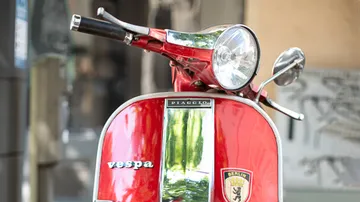 Rote Vespa steht in einer städtischen Umgebung, glänzend.