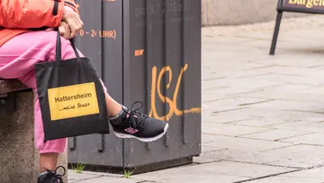 Schwarze Tasche mit Text sitzt neben einer Person auf einer Bank.