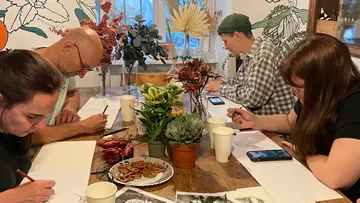 Four people draw with plants at a table.