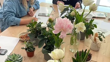 Flower arrangement on table, people drawing and writing down.