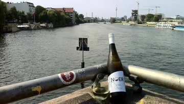 Eine Weinflasche und ein Glas stehen am Geländer.