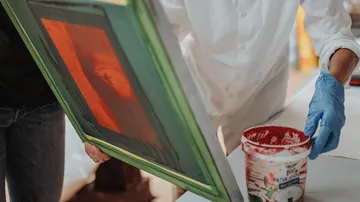 A silkscreen frame is dipped in paint.