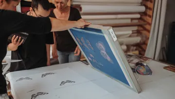 Printing frames are held over paper by people.