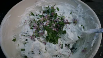 Schüssel mit Kräuterquark und frischen Blütenblättern.