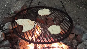 Teigwaren werden über einem Lagerfeuer auf einem Grill gebraten.