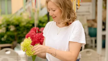 Frau hält frische grüne Blüten in der Hand, lächelt.
