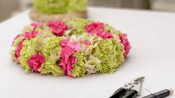 Wreath of flowers lying on table, tools next to it, bright environment.