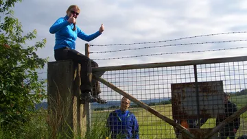 Woman sitting on fence, smiling, men standing in front of it.