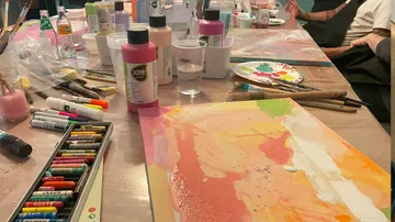 Bunt bemalte Leinwände liegen auf einem Tisch voller Farben.
