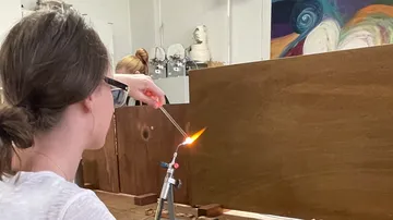 Frau schweißt mit einer Flamme Holz in einem Atelier.