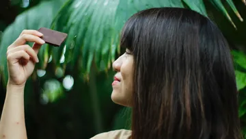 A woman is holding chocolate in the jungle and smiling.