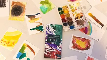 Watercolors and works of art are spread out on a table.