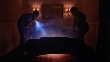 Zwei Männer untersuchen einen mysteriösen, rauchigen Bereich.