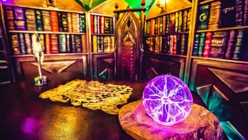 Kristallkugel leuchtet auf Tisch, umgeben von Bücherregalen.