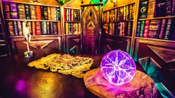 Purple ball on table surrounded by bookshelves and card.