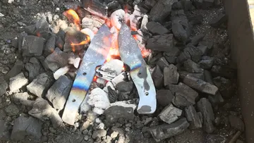 Metallteile glühen über einem Feuer in Kohlen.
