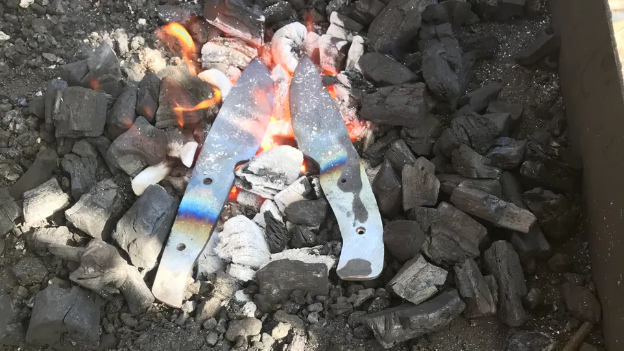 Metal parts glow in coals over a fire.