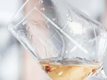 Ein geneigtes Glas mit goldenem Getränk in unscharfer Umgebung.