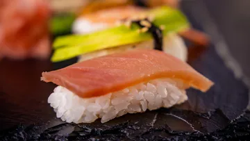 Sushi roll is placed on black plate, fresh tuna surface.