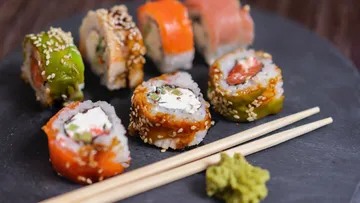 Colourful sushi rolls lie on a black plate.
