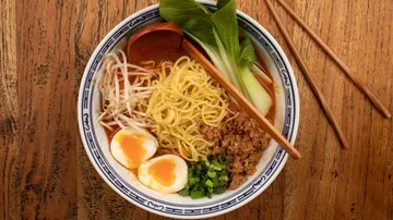 A bowl of ramen with eggs, vegetables and ground beef.