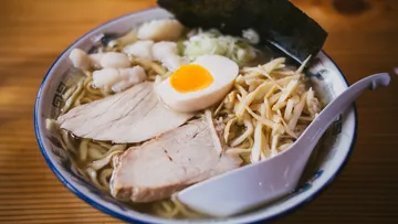 Bowl of ramen filled with ingredients on a wooden background.