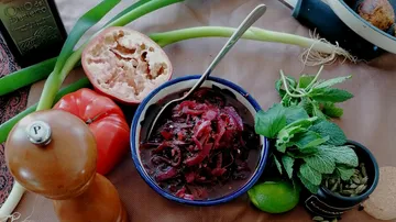 Bowl of red vegetables and herbs surrounded by ingredients.