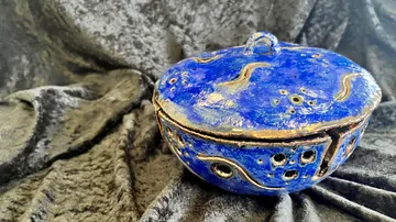 Eine blaue Schale steht auf schwarzem, samtigem Stoff.