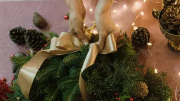 Hands tie a bow around an advent wreath, festively decorated.
