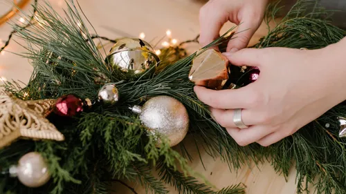 Hands decorate a green Christmas wreath with balls.