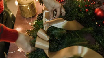 Hands tie a bow around a Christmas wreath.