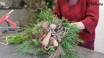 Frau gestaltet einen dekorativen Kranz aus Naturmaterialien.