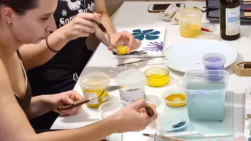 Two people paint with brushes and paints on a table.