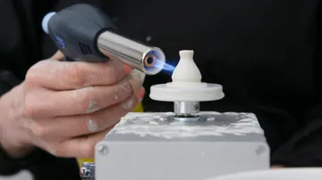 Eine Hand hält einen Brenner, der ein Drehobjekt erhitzt.